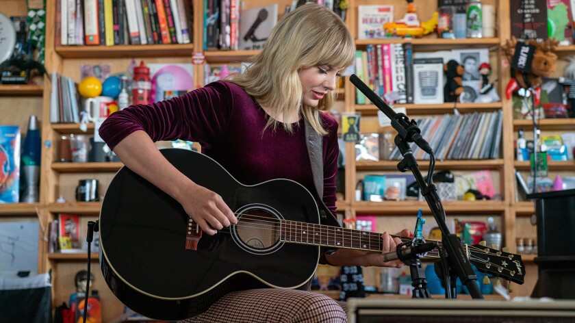 Taylor Swift plays guitar in front of a bookcase.