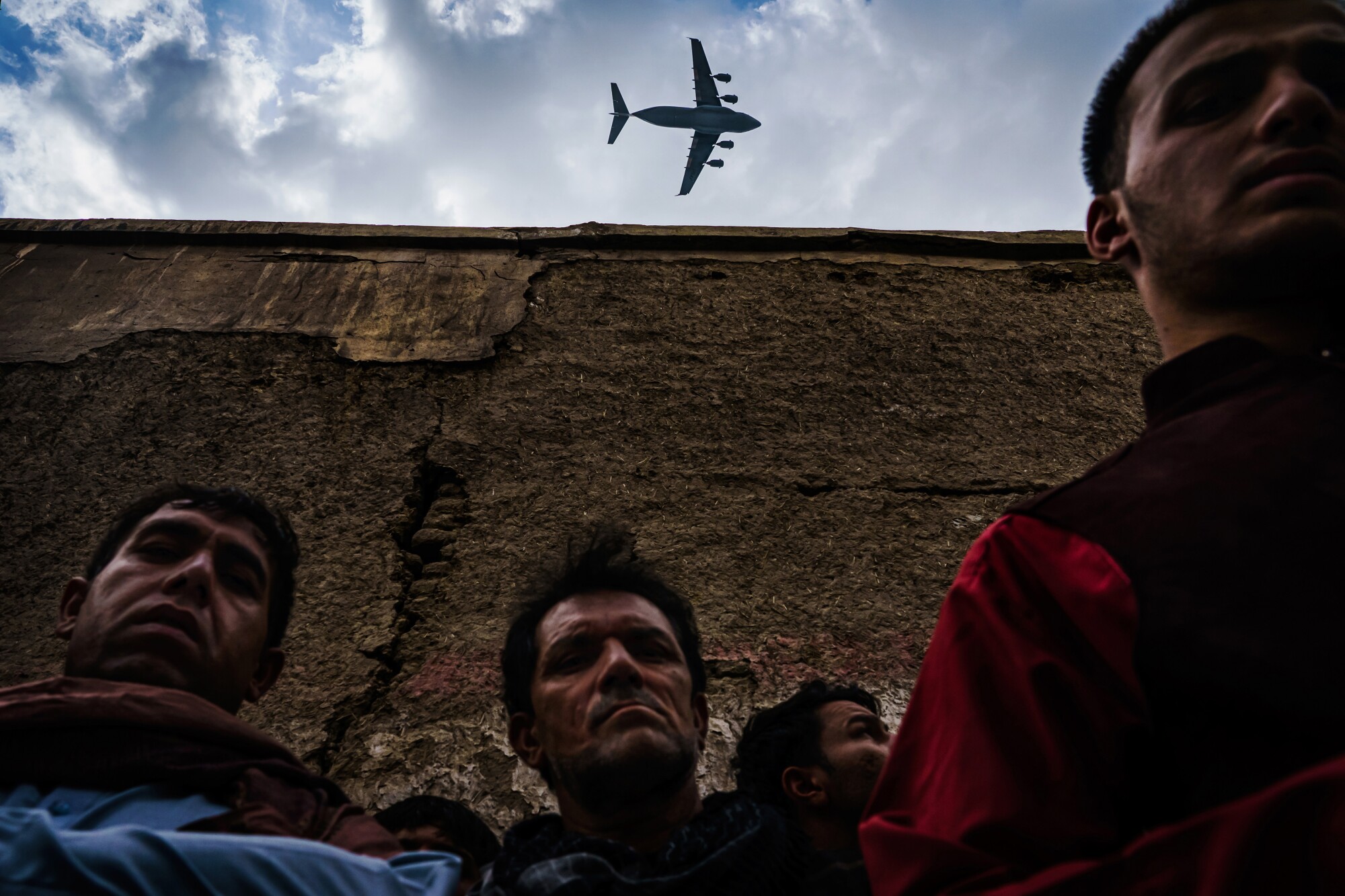 A military transport plane flies over men in the foreground.