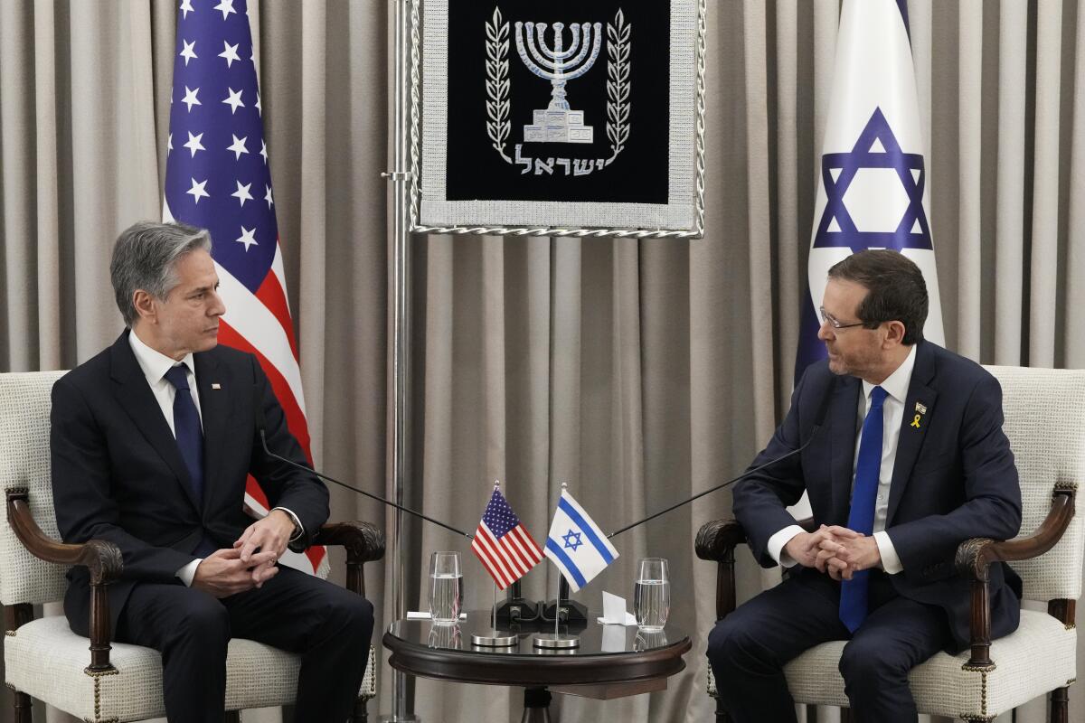 Secretary of State Antony Blinken sits with Israeli President Isaac Herzog with U.S. and Israeli flags in the background. 