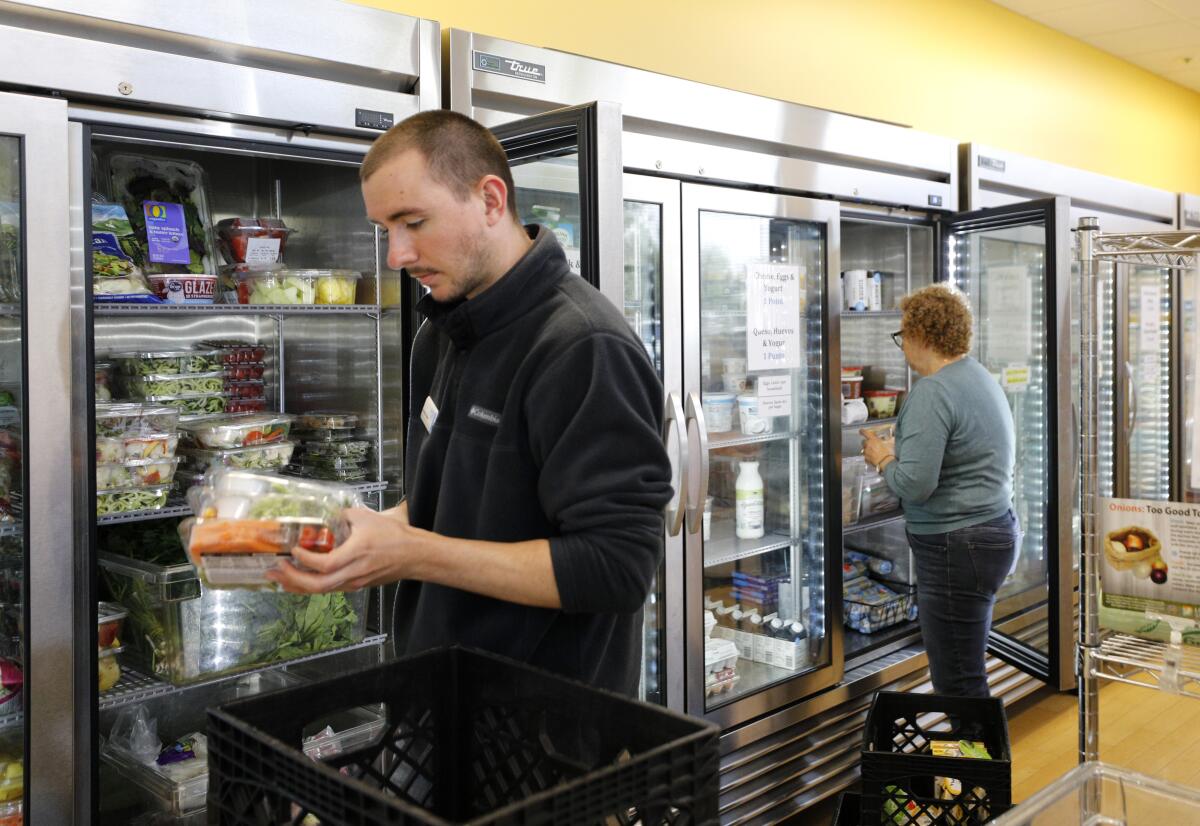 A man and a woman restock a refrigerator case.