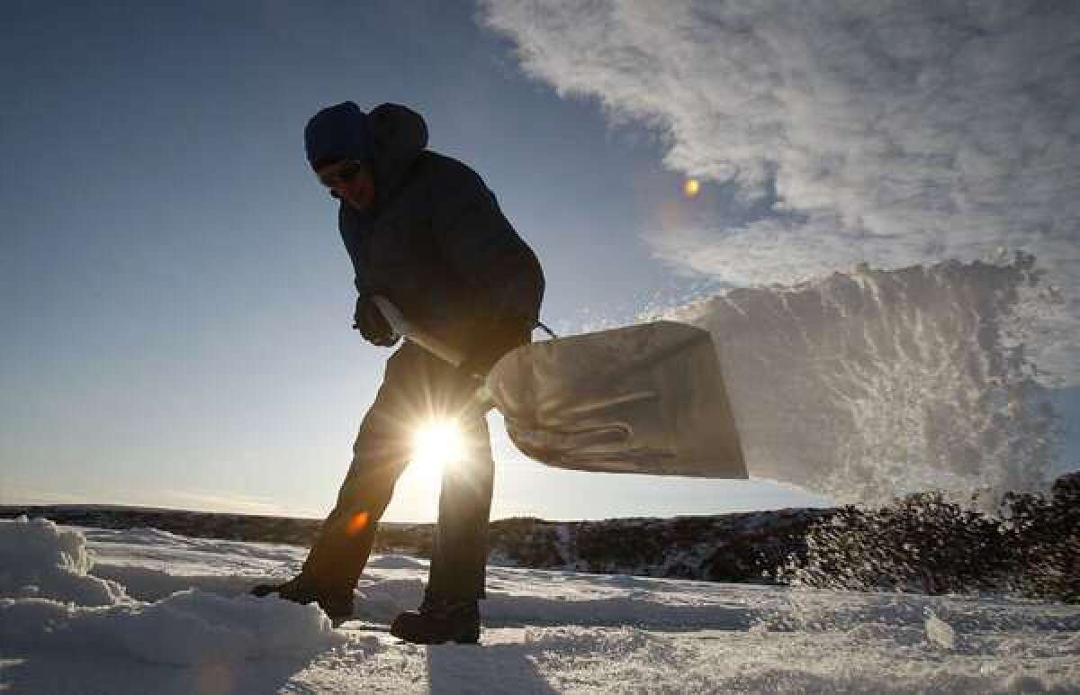A researcher shovels snow from the surface of a frozen tundra lake in search of frozen bubbles that indicate a seep of methane gas, which is created when microbes digest organic material contained in permafrost.