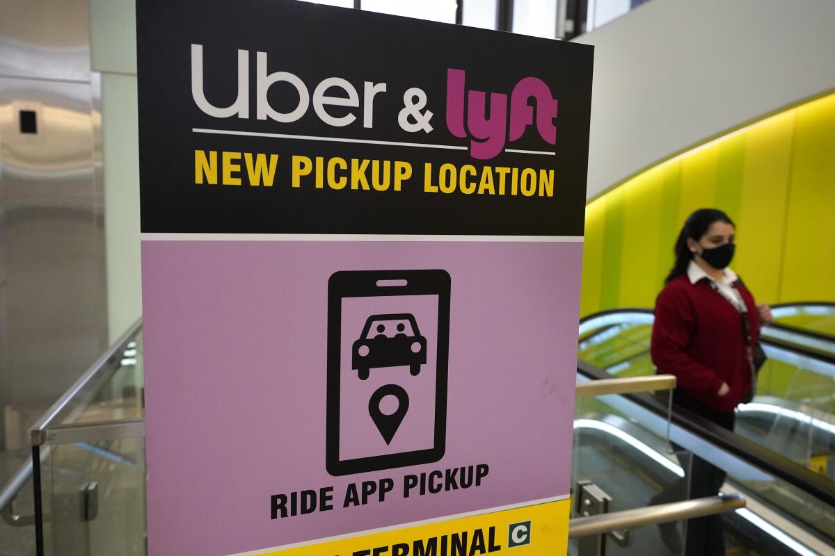 A passer-by walks past a sign offering directions to an Uber and Lyft ride pickup location at Logan International Airport, in Boston, Tuesday, Feb. 9, 2021. Uber and Lyft are taking different routes around the roadblock the virus pandemic dropped on their paths to profitability. The companies have racked up tens of billions of dollars in losses since starting up, and the slump in passenger activity has pushed profitability ever further off into the future. (AP Photo/Steven Senne)
