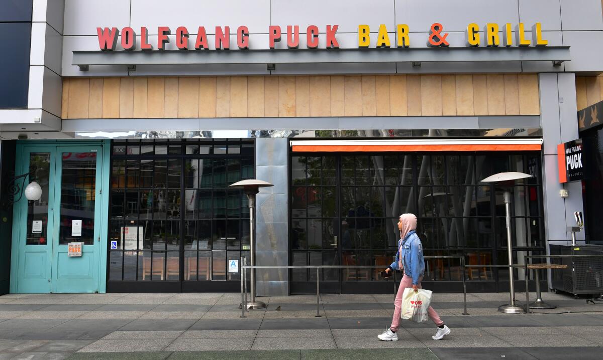 A pedestrian walks past a closed Wolfgang Puck Bar & Grill restaurant in Los Angeles. To slow the coronavirus epidemic, dine-in services has been halted at the city's restaurants.
