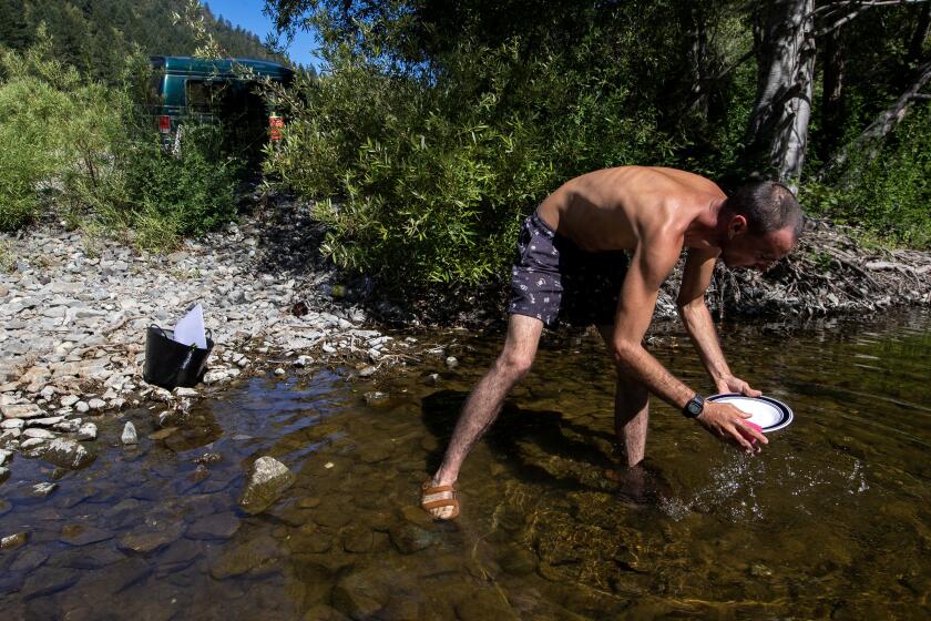 COVELO, CA - June 24, 2022 Cristiano washes dishes in the Eel River on Friday, June 24, 2022 in Covelo, CA. Cristiano, is owed $30,000 from a legal grower who stiffed him after working 6 months on a cannabis farm in Covelo, CA. The undocumented immigrant from Portugal says he can't go home with nothing, and vows to stay until he is paid. He is living in his van and is almost broke. UPDATE - He has since sold his van and is looking to leave the country. (Brian van der Brug / Los Angeles Times)