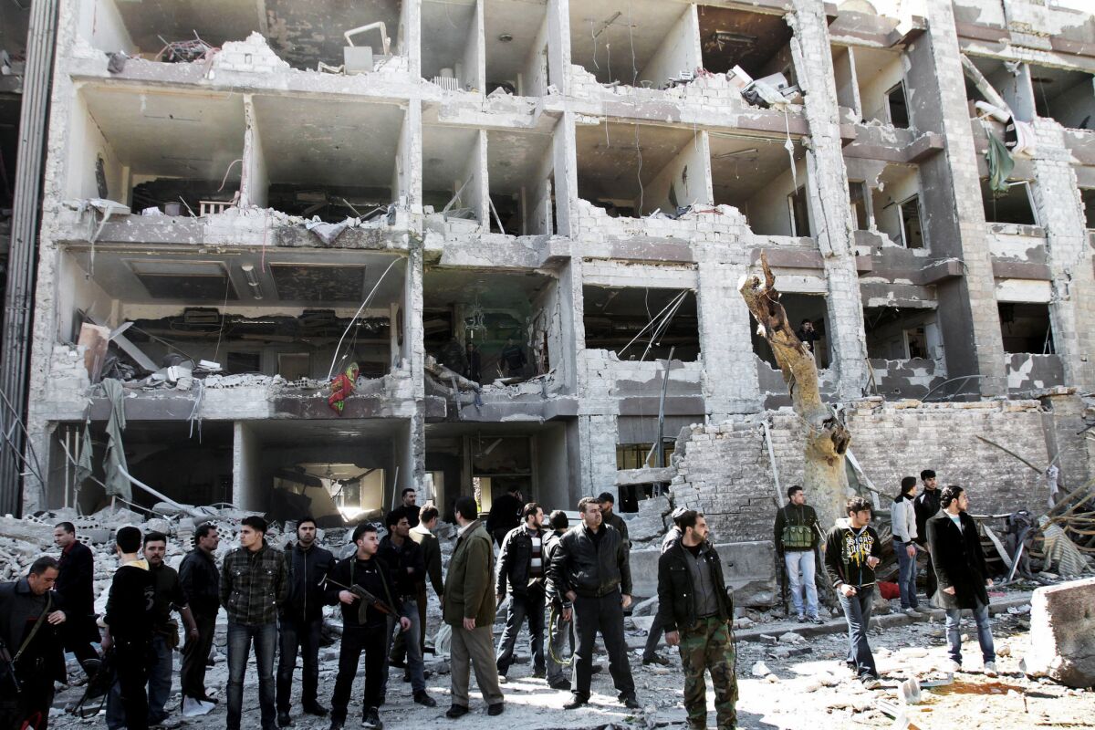 Syrian security officers gather March 17 in front of the damaged building of the aviation intelligence department, which was hit by one of two explosions in Damascus. Jabhat al-Nusra claimed that it carried out the double suicide bombing.