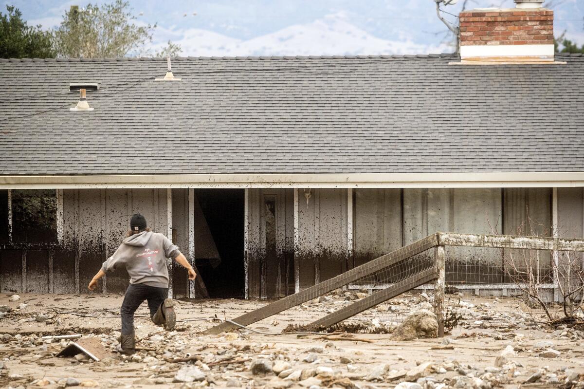 A man crosses mud toward a Monterey County home damaged in a mudslide.