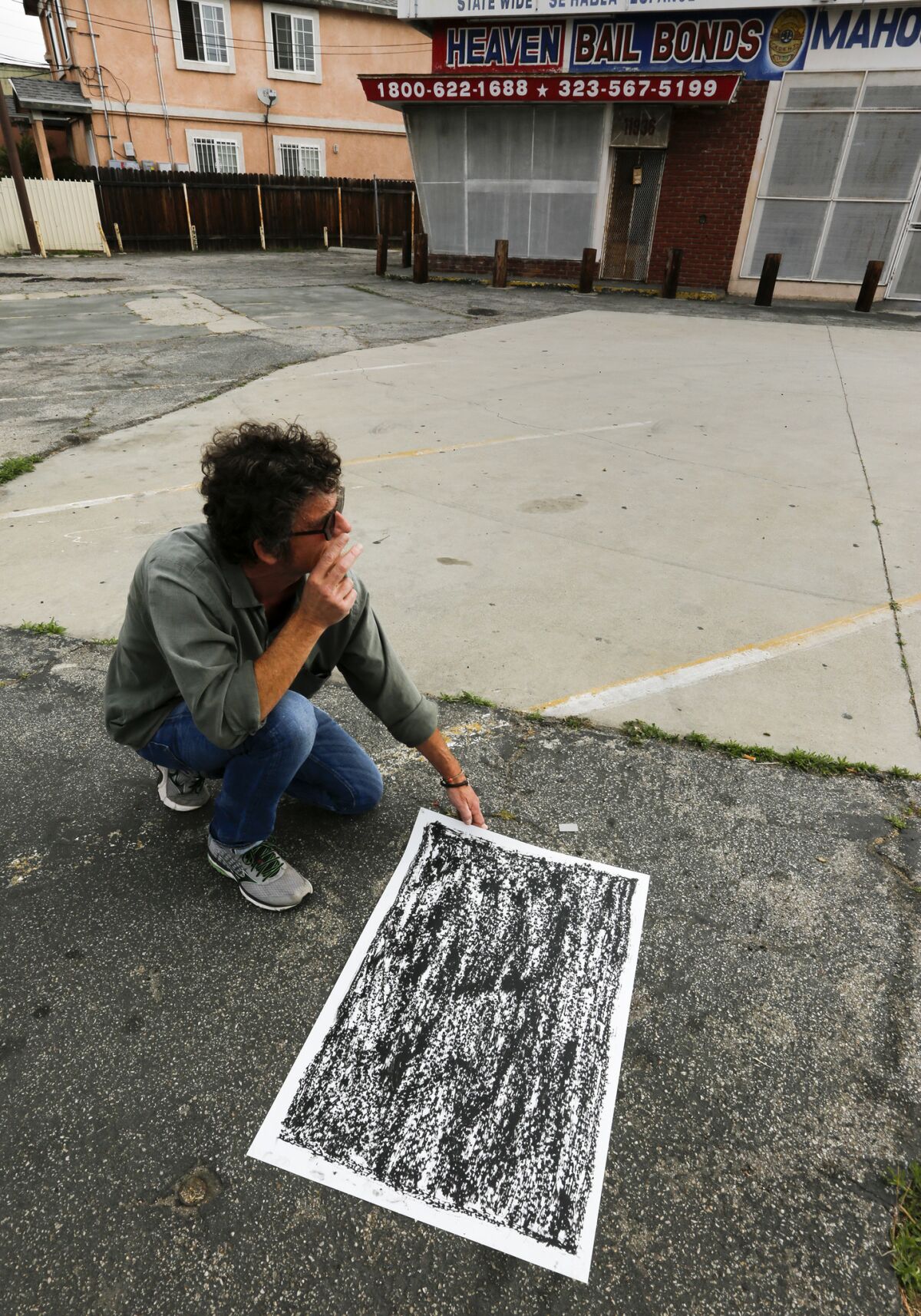 Artist Jeff Beall at the corner of Central Avenue and East 120th Street, in community of Green Meadows, with a rubbing that marks the site of an unsolved death. (Mark Boster / Los Angeles Times)