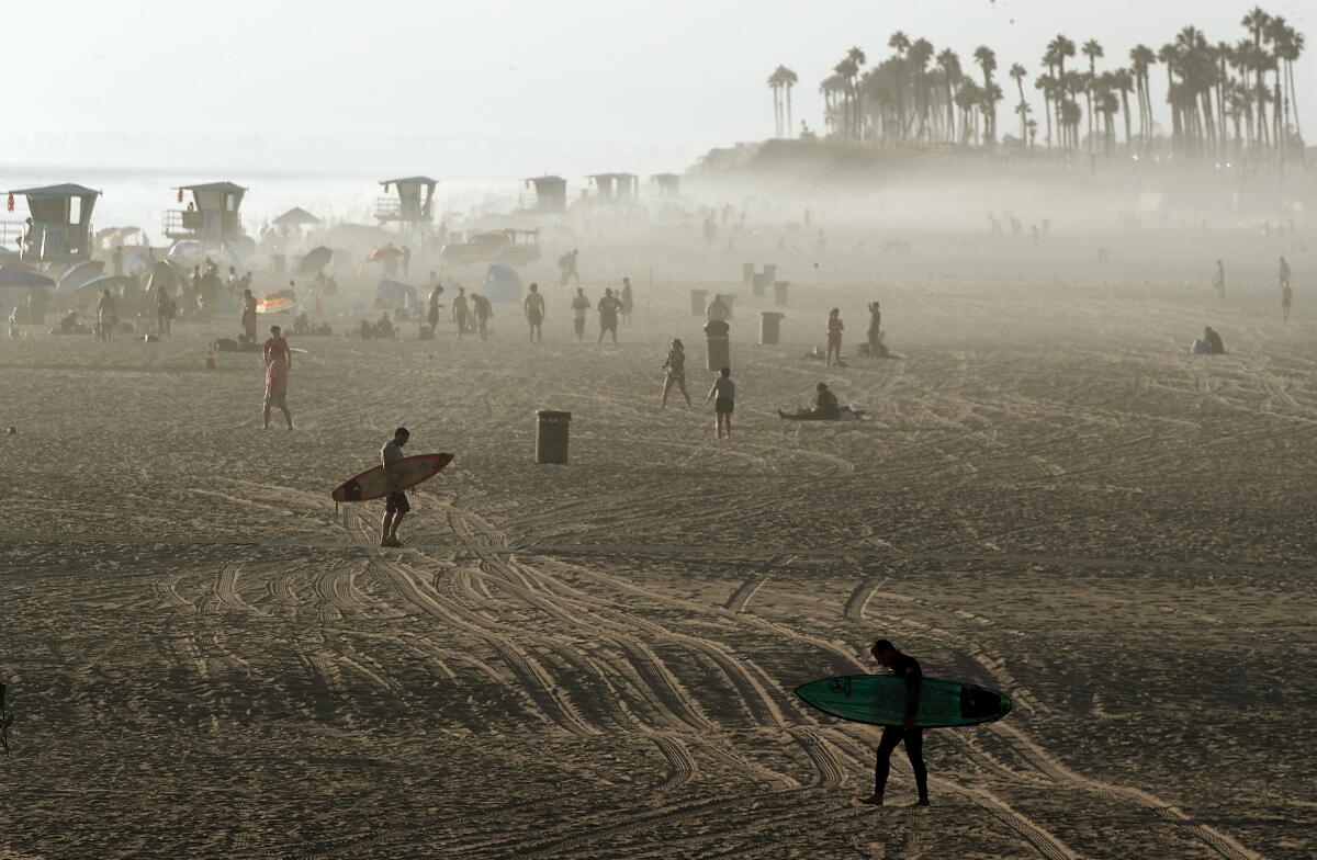 Surfers walk across the sand as fog drifts ashore at sunset at Huntington Beach