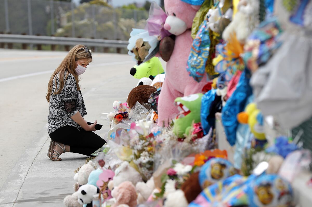 A visitor kneels at a memorial shrine in honor of Aiden Leos on an overpass above the 55 Freeway in Orange.