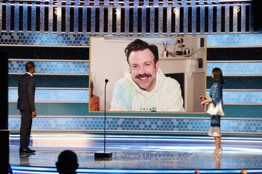 Jason Sudeikis smiling in a sweatshirt on a big screen at the Golden Globes