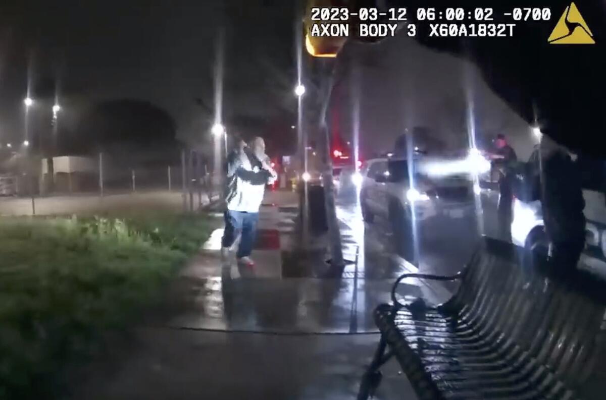 A man holds up a metal pole as he runs toward police officers with weapons drawn