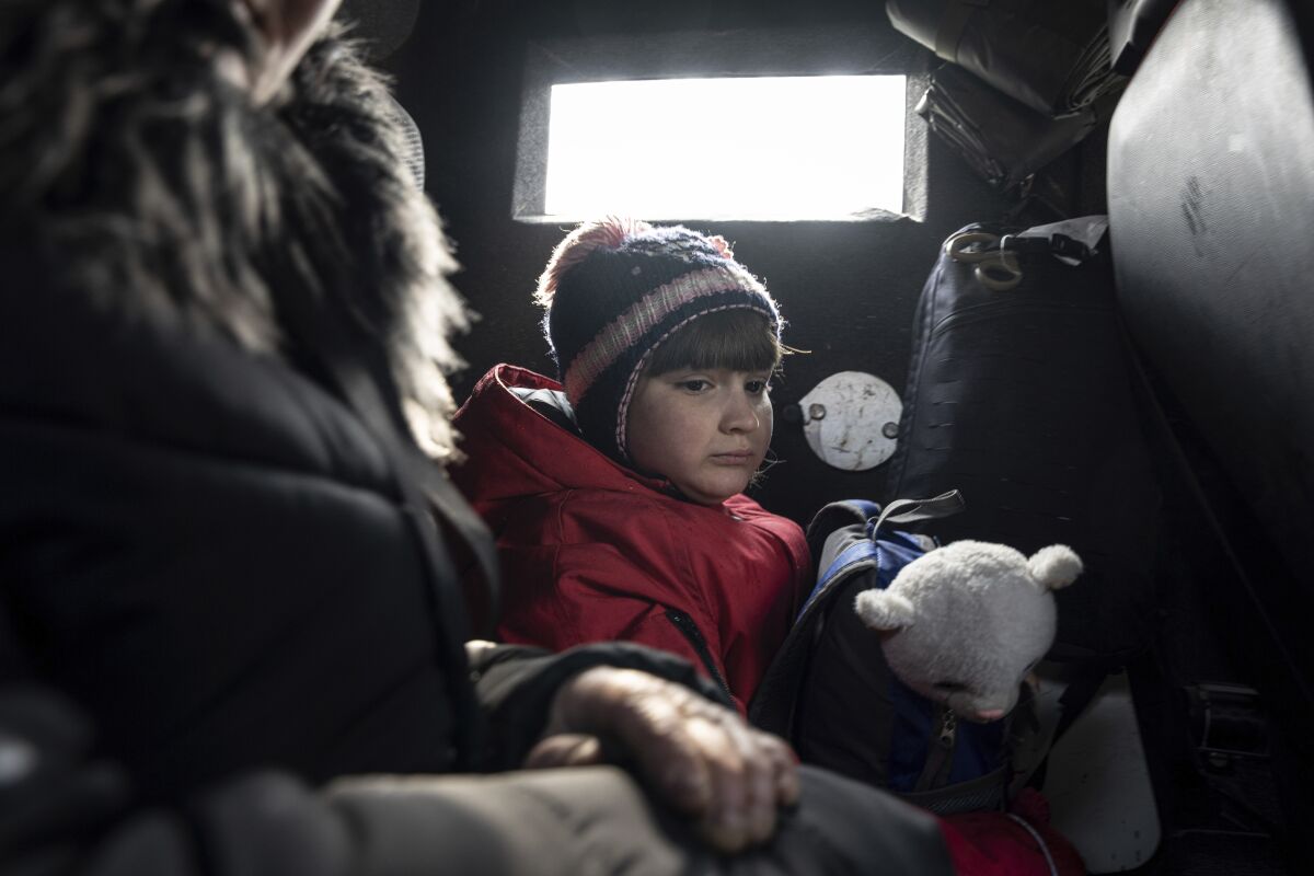A girl rides with her mother in a van during evacuation by Ukrainian police, in Avdiivka, Ukraine, Tuesday, March 7, 2023. For months, authorities have been urging civilians in areas near the fighting in eastern Ukraine to evacuate to safer parts of the country. But while many have heeded the call, others -– including families with children -– have steadfastly refused. (AP Photo/Evgeniy Maloletka)