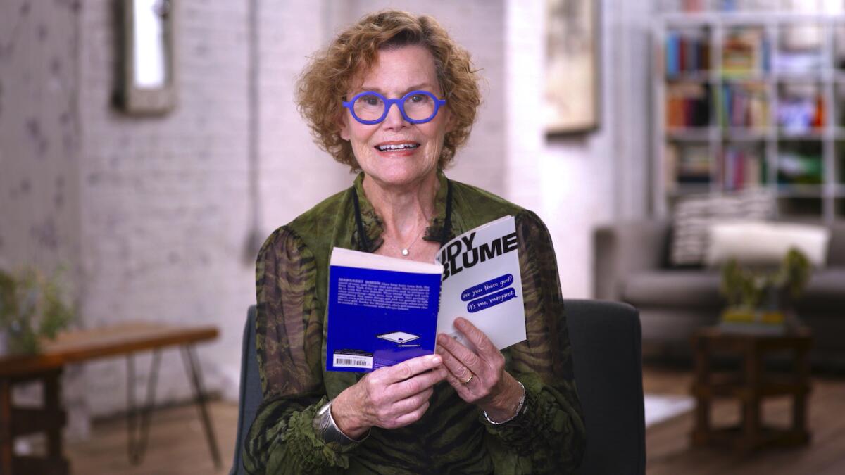 a woman wearing bright blue glasses holds a book 