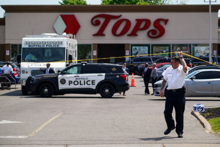 A police officer lifts the tape cordoning off the scene of a shooting at a supermarket, in Buffalo, N.Y., Sunday, May 15, 2022. A white 18-year-old wearing military gear and livestreaming with a helmet camera opened fire with a rifle at a supermarket in Buffalo, killing and wounding people in what authorities described as “racially motivated violent extremism.” (AP Photo/Matt Rourke)
