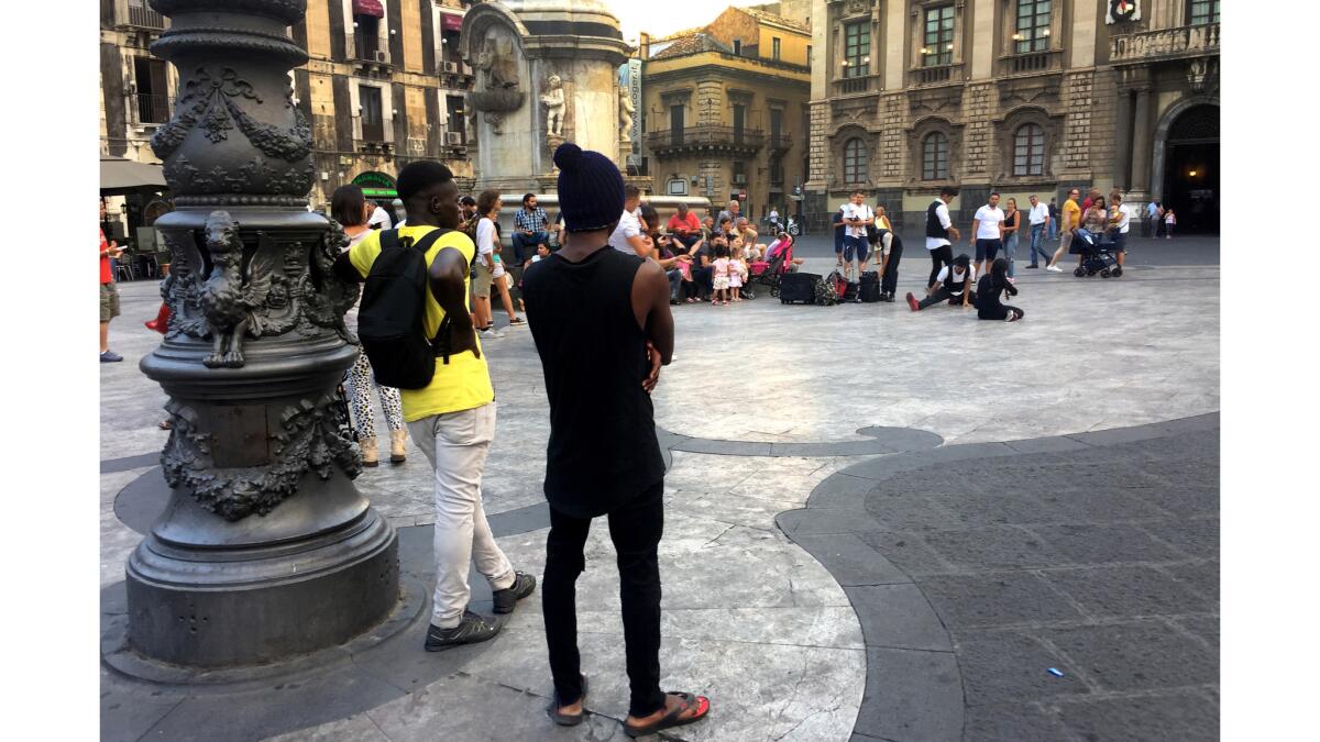 Two young migrants watch street performers in Catania's Piazza del Duomo.