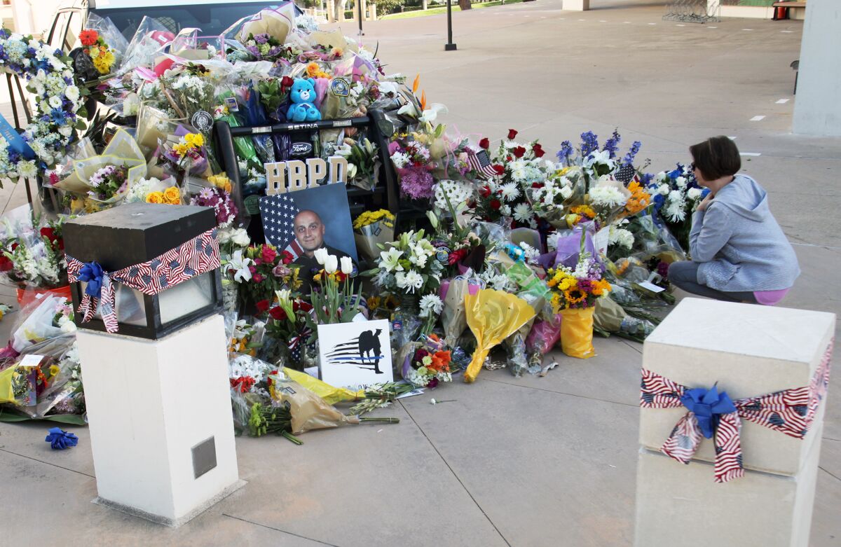 A woman kneels in front of a mound of flowers, photos and other memorial items