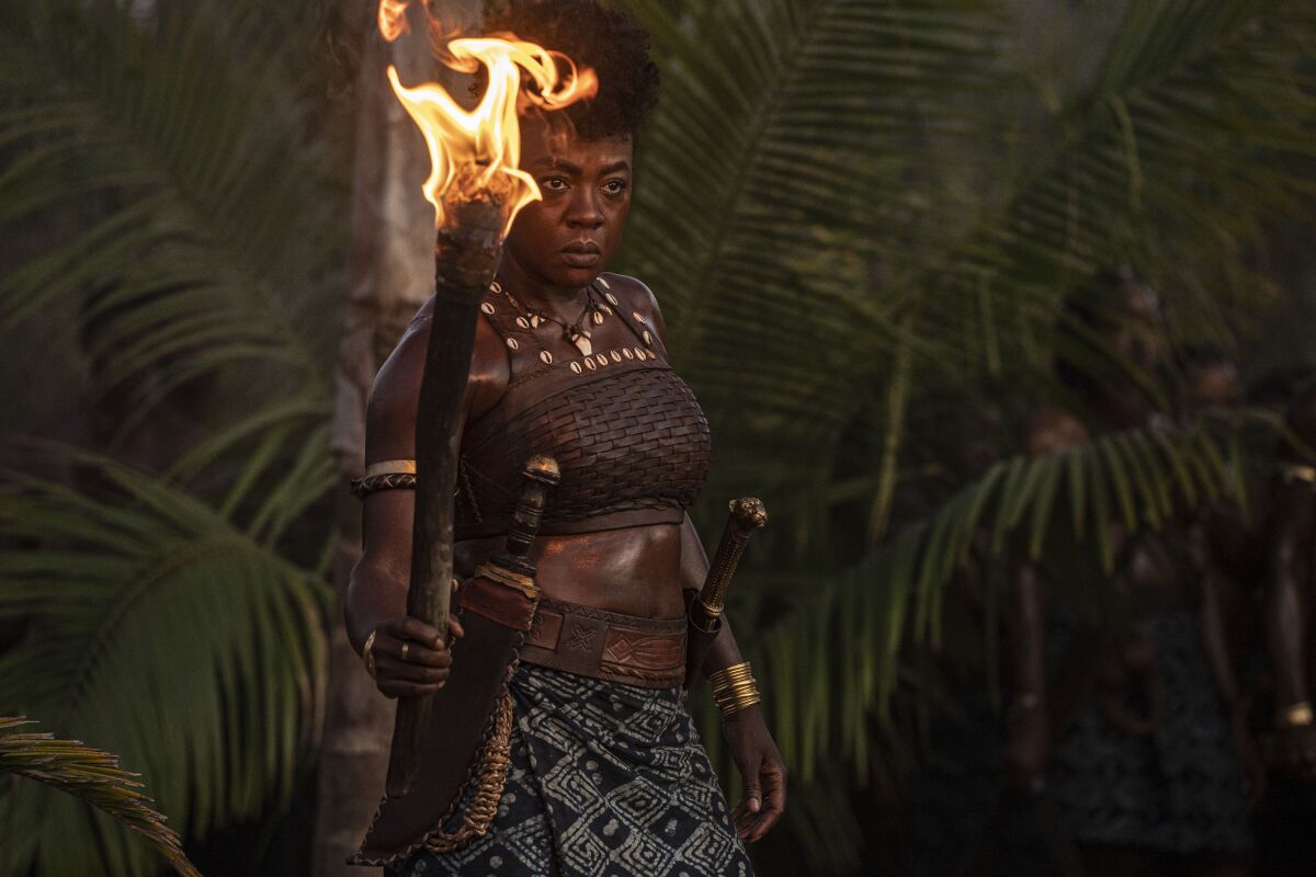 A fierce-looking woman stands holding a flaming torch.