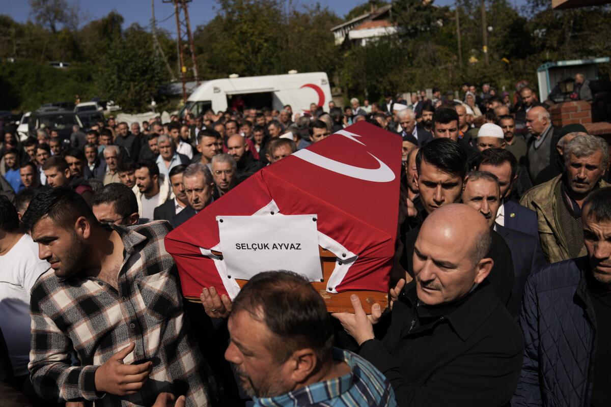 Turkey's Interior Minister helps carry a coffin covered with a Turkish flag while surrounded by many people.