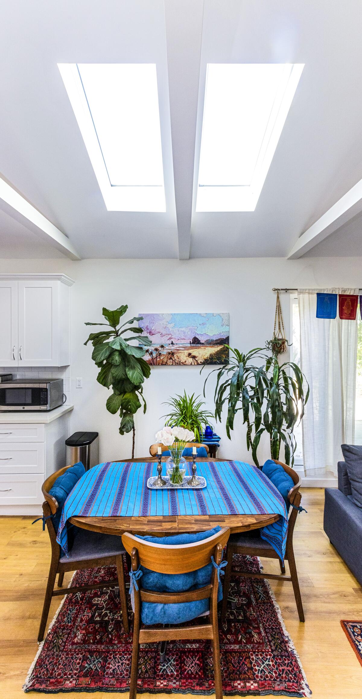 Light shines through skylights above a kitchen table with tall houseplants in the background.