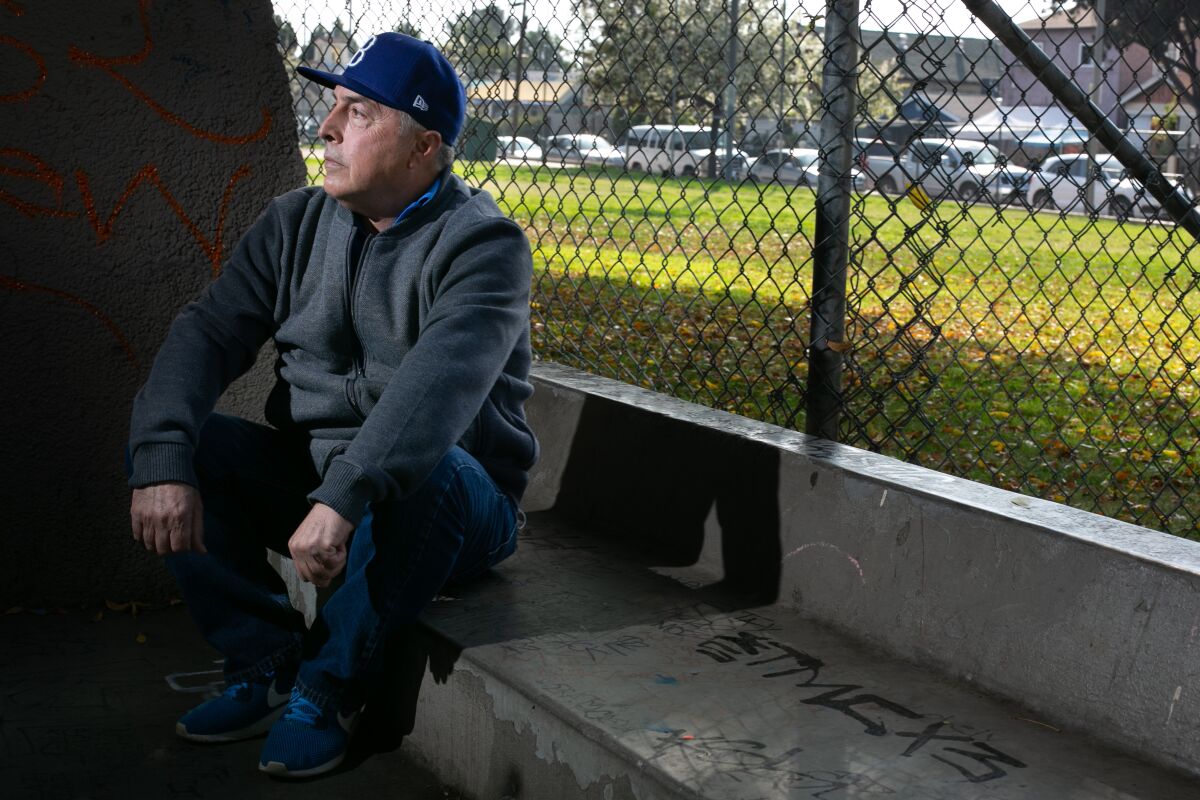 A man poses for a portrait, sitting on a concrete bench at a park