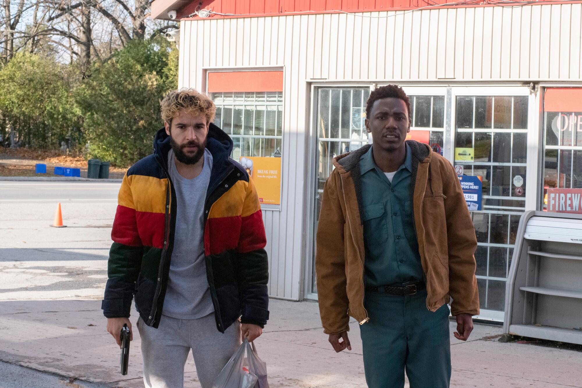 Two men, the one on the left holding a gun, outside a convenience store 