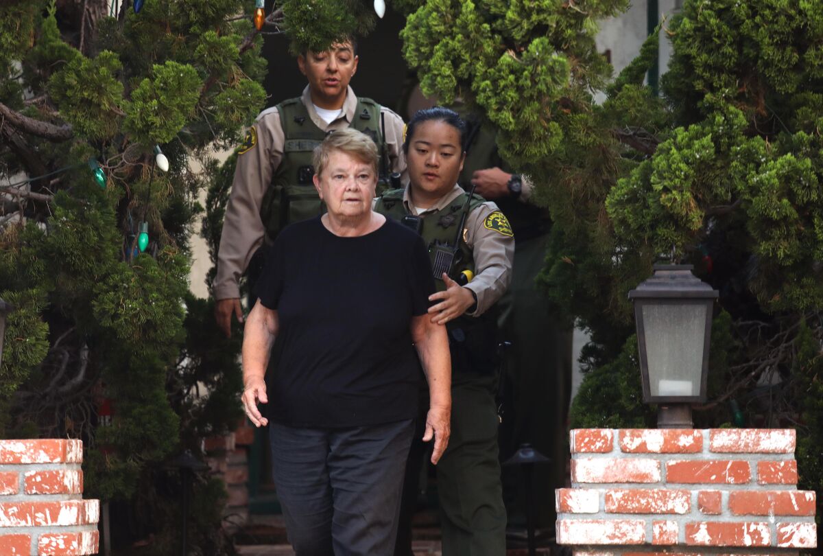 A woman walks outside a home with law enforcement officers.