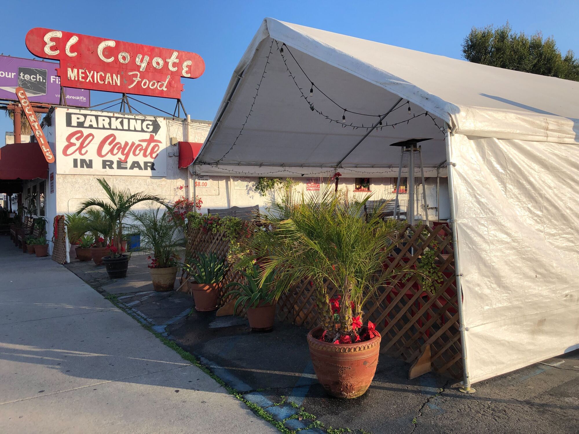 A white party tent is seen in the foreground of El Coyote's retro Modernist signage, which rises above the building