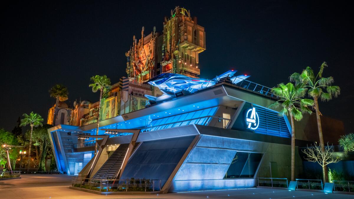 A large metallic structure lighted in blue with the Avengers logo in front of the Guardians of the Galaxy tower