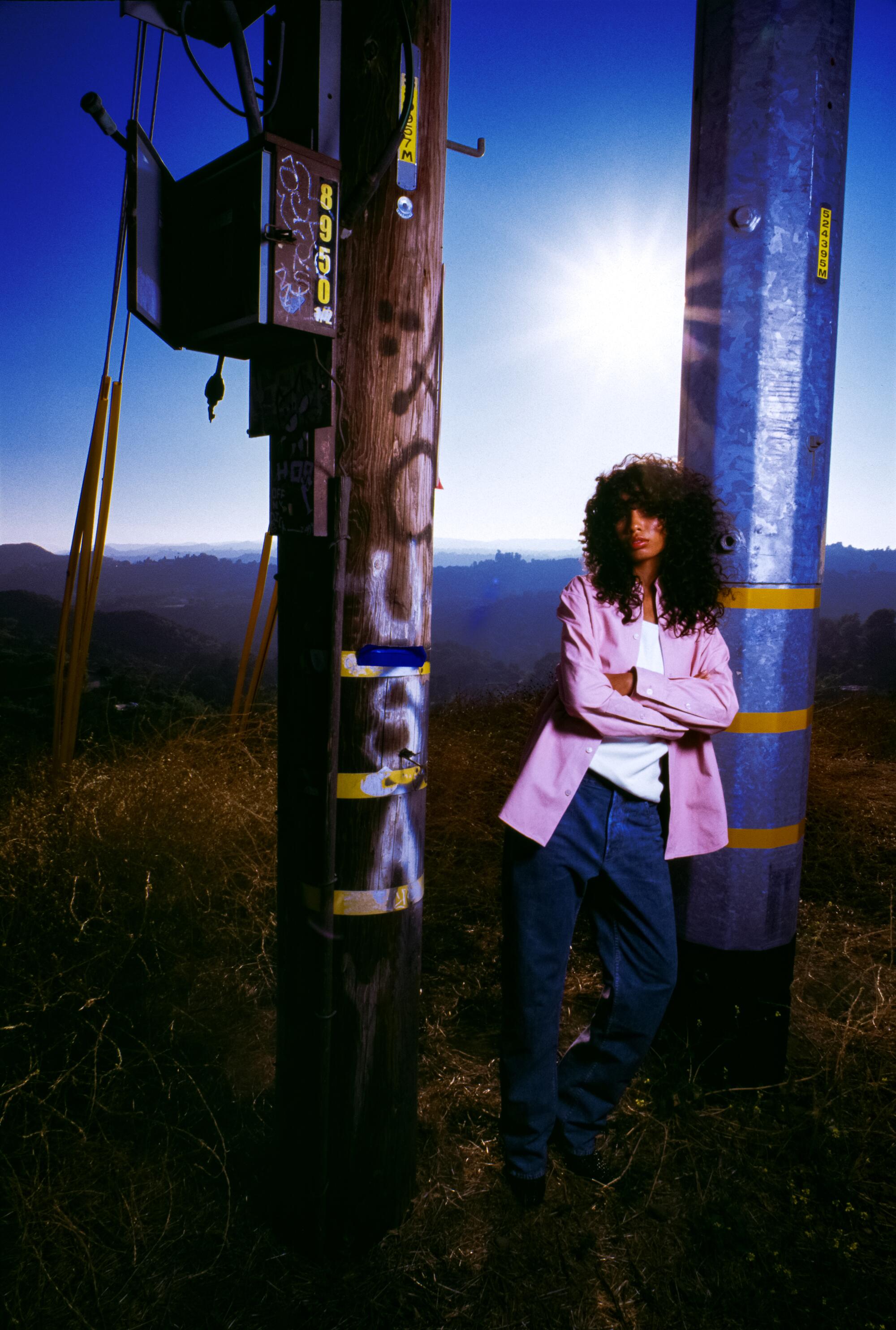 A model in a pink jacket leans against a signpost with the San Fernando Valley spread out behind her