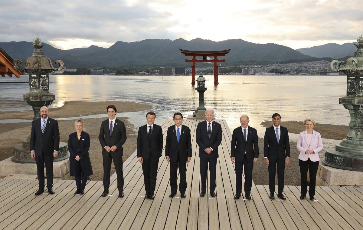 World leaders are shown in front of a lake with a Japanese shrine placed amid the water. 