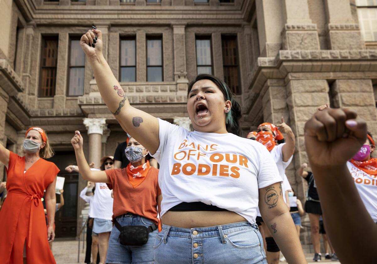 People at a rally raise their fists and shout outside a building.