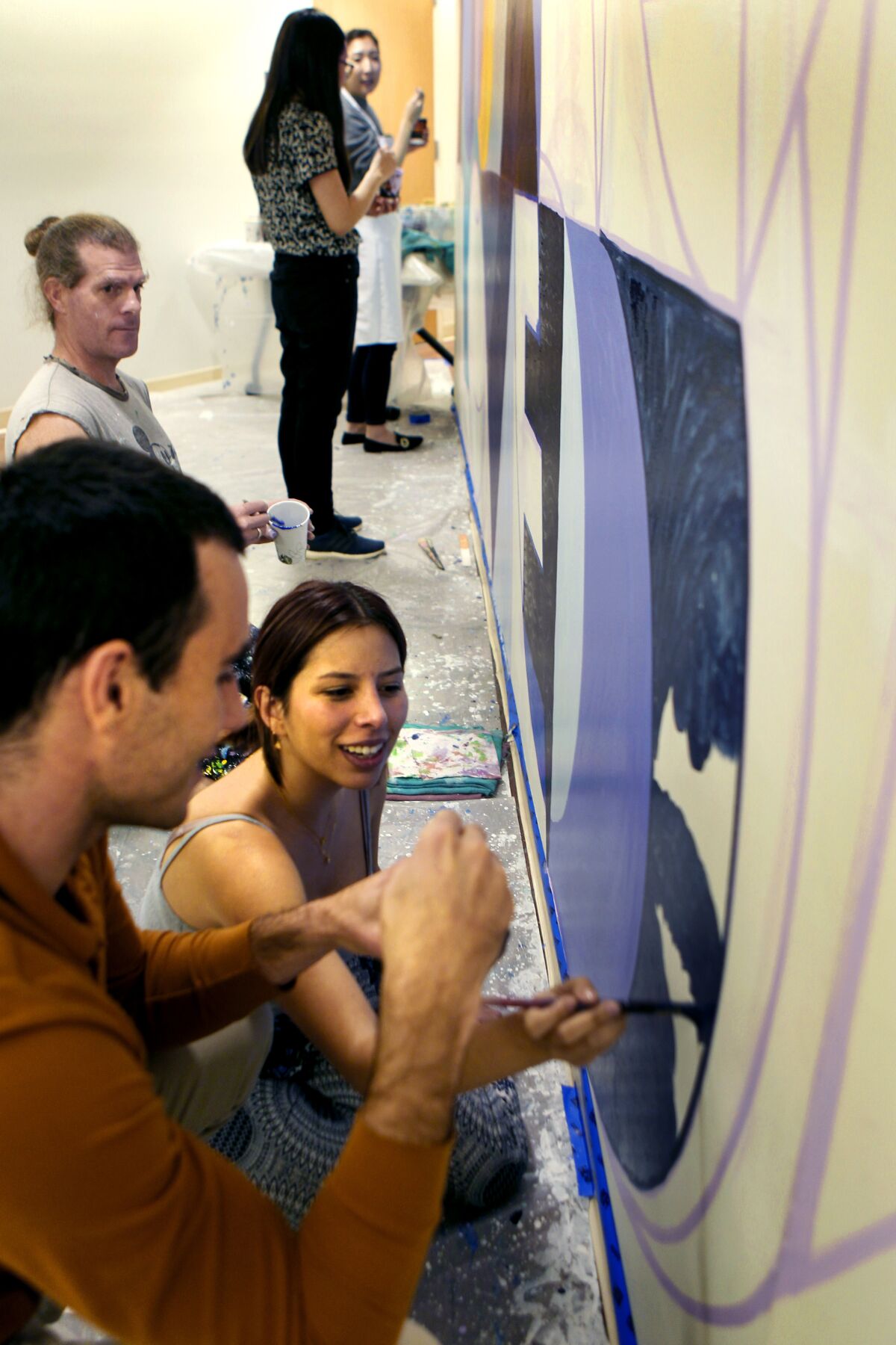 Artist Alex Cook supervises as Ph.D. student Benji Kaveladze, foreground, and undergrad Jaclyn Gonzalez help paint Cook's "You Are Loved" mural in the Social Ecology I building at UC Irvine. The mural is part of the School of Social Ecology's Compassion Action Project.