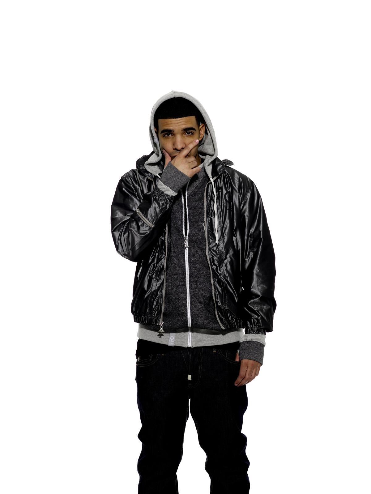 Drake, in a hoodie and jacket, stands with his hand covering his mouth.