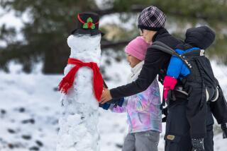 Mt. Baldy, CA - January 03: Amelia Dinh, 7, left, and mom Mai Dinh, right, put the finishing touches on a snowman along Mt. Baldy Rd. on Wednesday, Jan. 3, 2024 in Mt. Baldy, CA. (Brian van der Brug / Los Angeles Times)