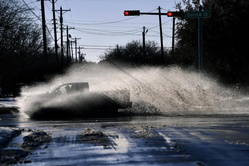 A pickup sends a wake of snow melt high into the air as the driver plows through a large puddle at Barrow and South 11th streets intersection in Abilene, Texas, Friday, Feb. 19, 2021. Temperatures climbed above freezing for the first time since Sunday's record 14.8-inch snowfall. (Ronald W. Erdrich, The Abilene Reporter-News via AP)