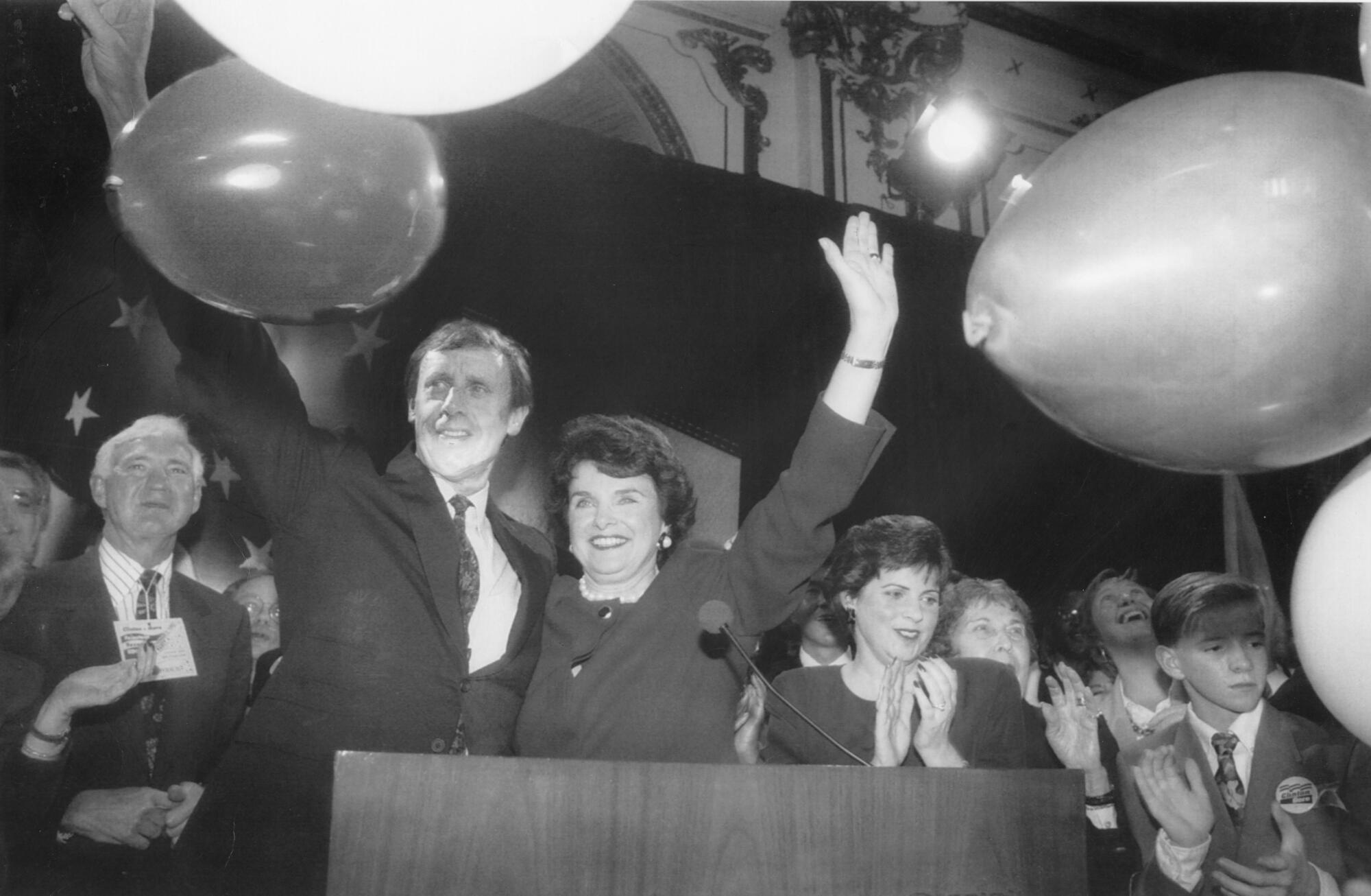 A black-and-white photo of Dianne Feinstein and third husband Richard Blum onstage at a rally with her daughter, Katherine.