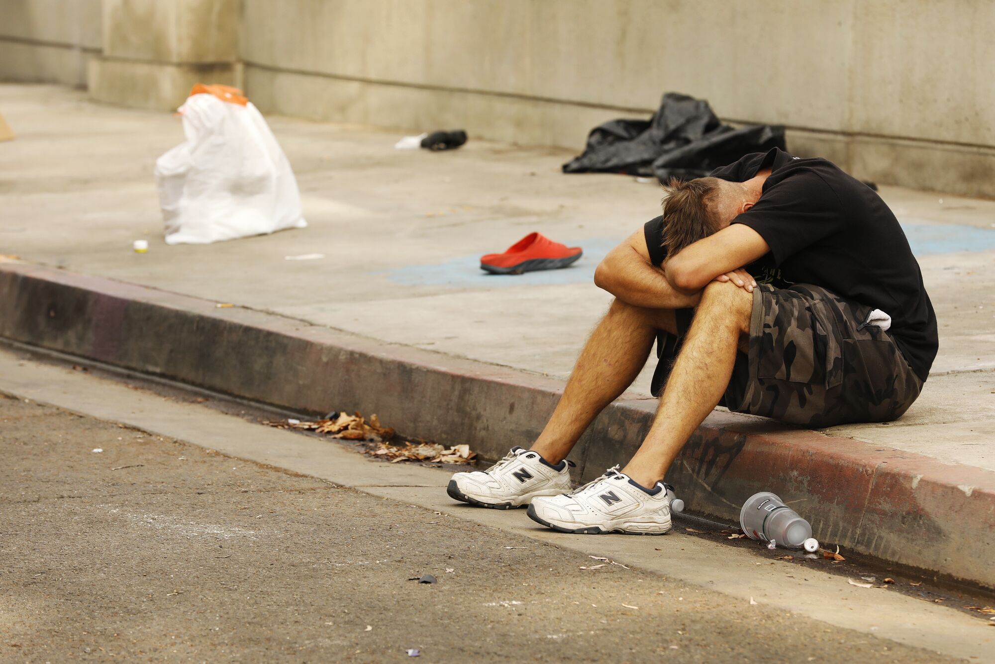 A man sitting on a curb has his head down between his arms and legs.