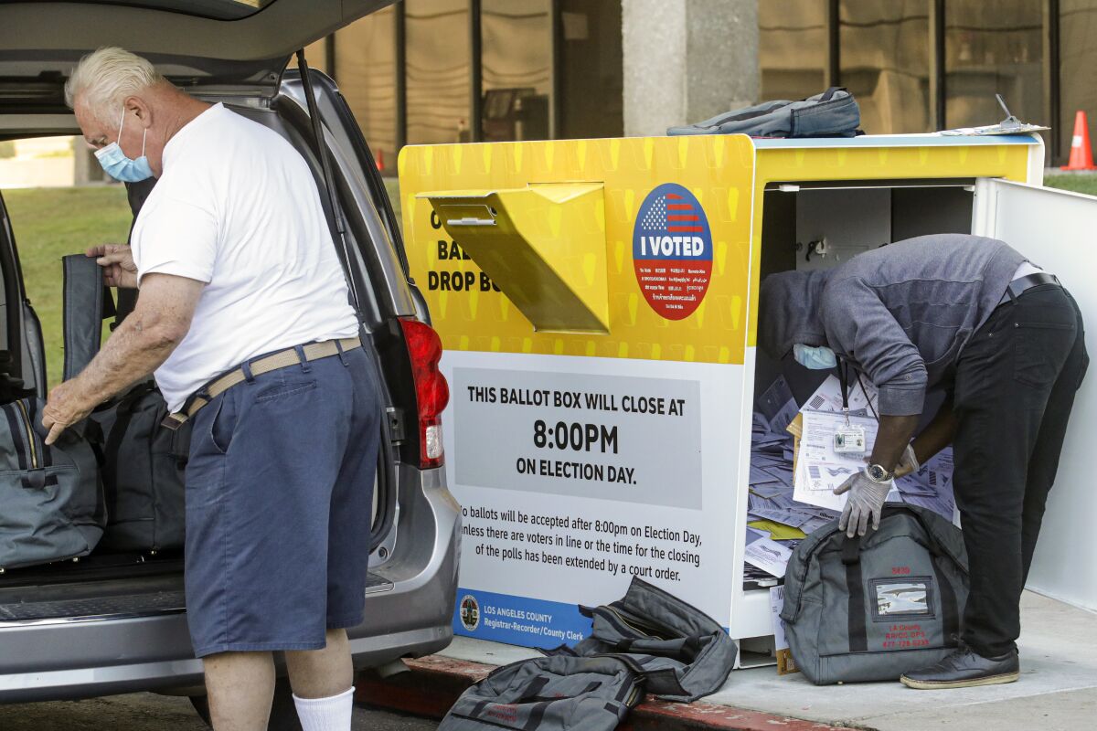 A worker bends over to move ballots from a drop box into gray bags as another worker loads bags into the back of a van