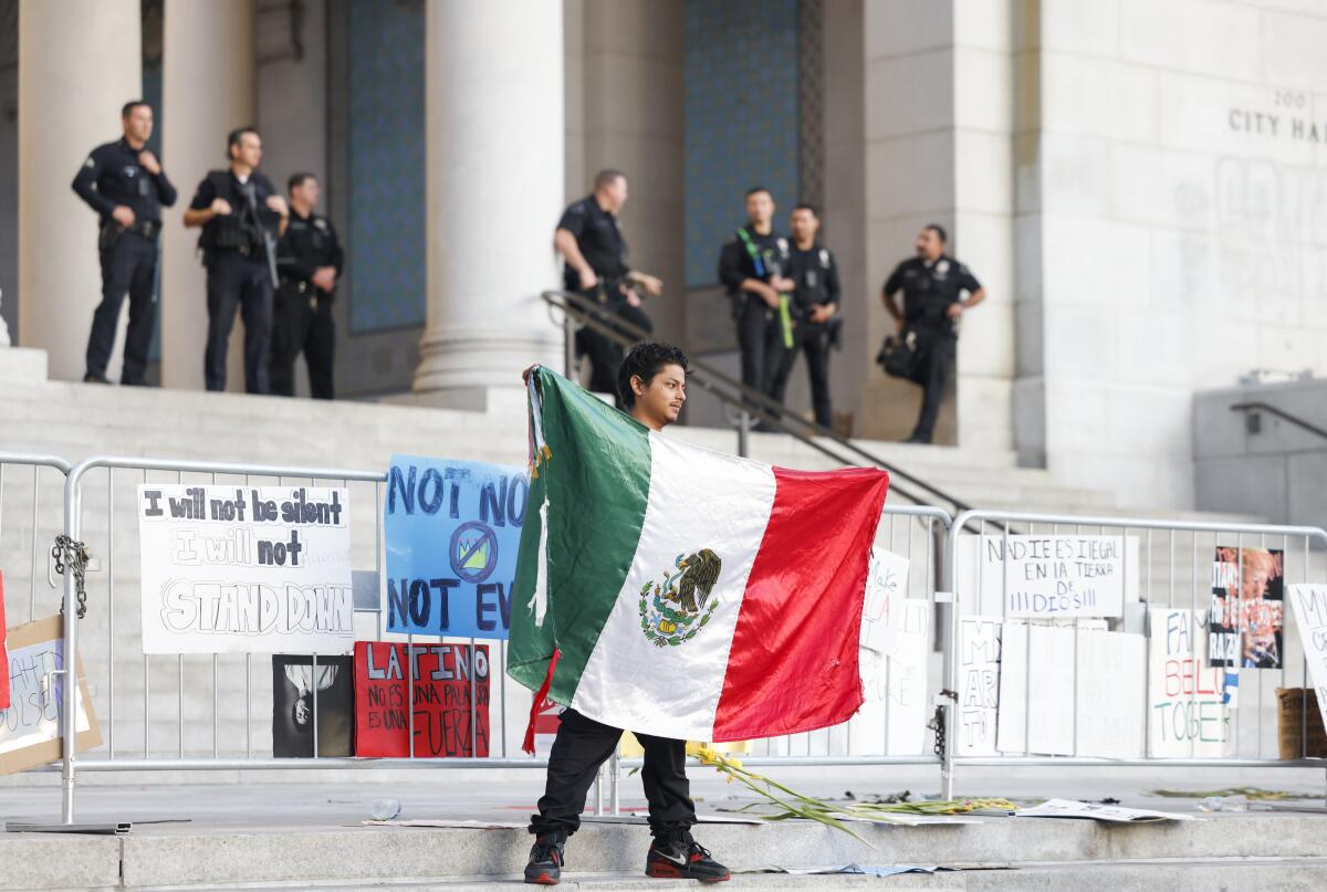 A man holds a Mexican flag in front of City Hall.