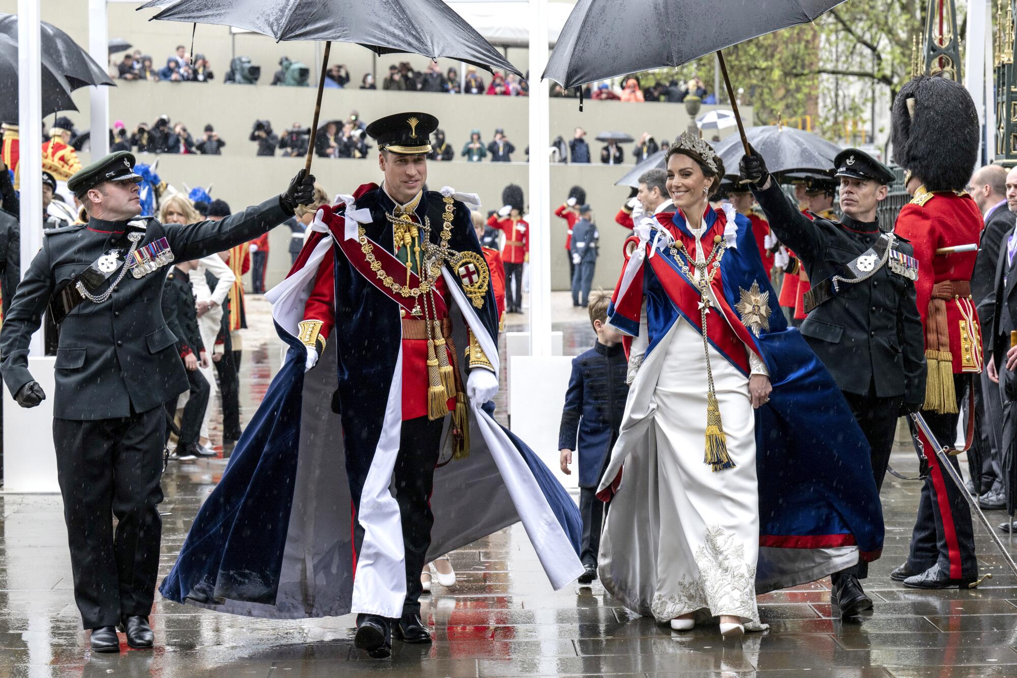 Britain's Prince William and Kate, Princess of Wales walk together, shielded from rain by two officers holding umbrellas
