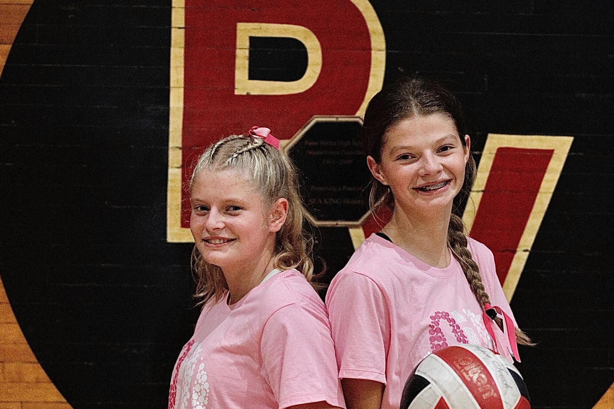 Twins Molly and Mallory LeBreche stand back to back each holding a volleyball.