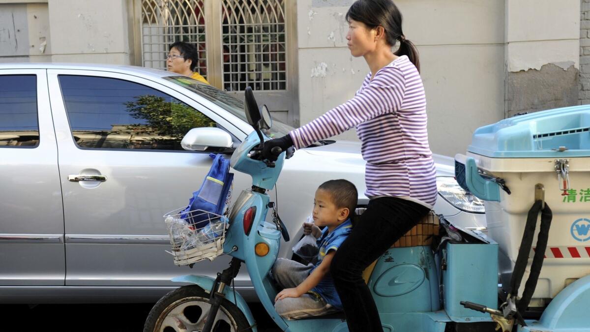 A mother rides an electric tricycle along a street in Tianjin with her son.