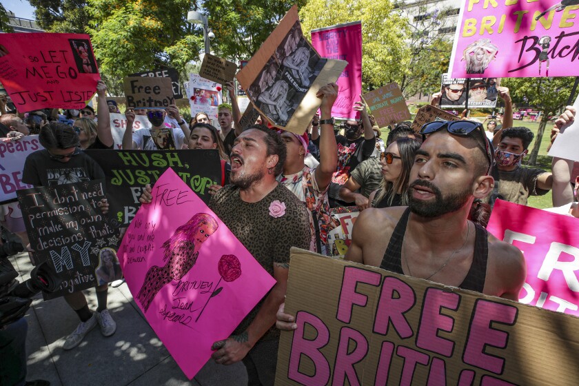 A crowd of people shouting and waving pink, black and brown signs