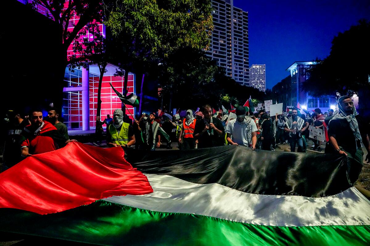 Protesters march in the street behind an enormous Palestinian flag.