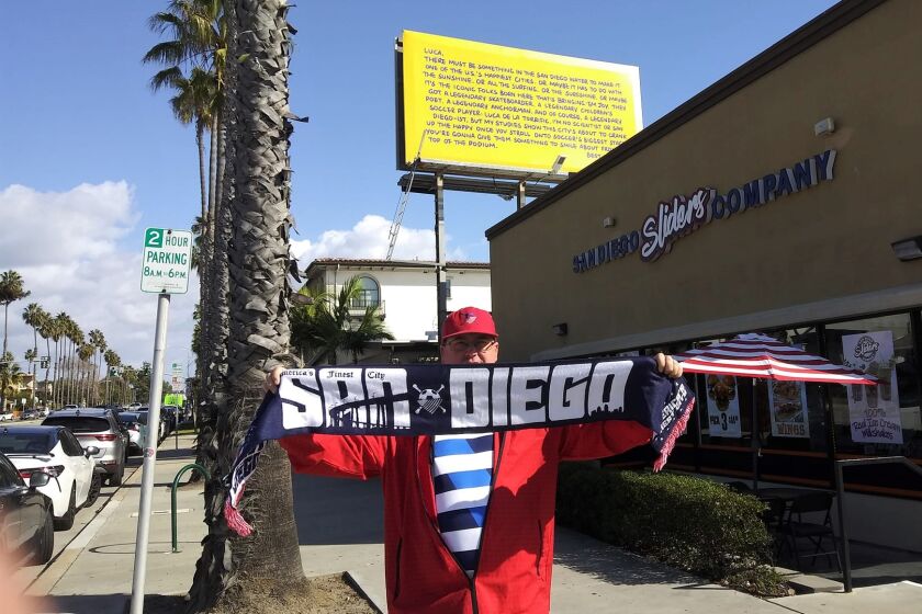 David Chamberlain, head of a S.D. soccer support group, stands below Ted Lasso's Pacific Beach billboard to Luca de la Torre.