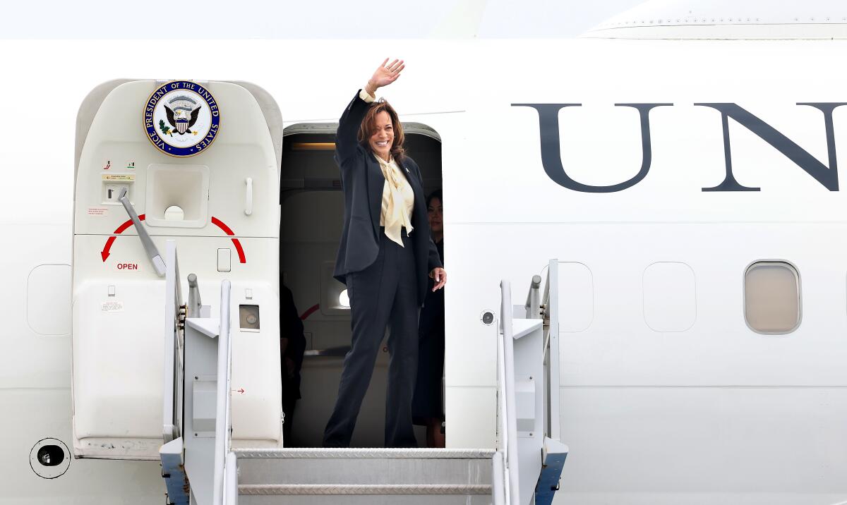 Vice President Kamala Harris waves from an airplane door.