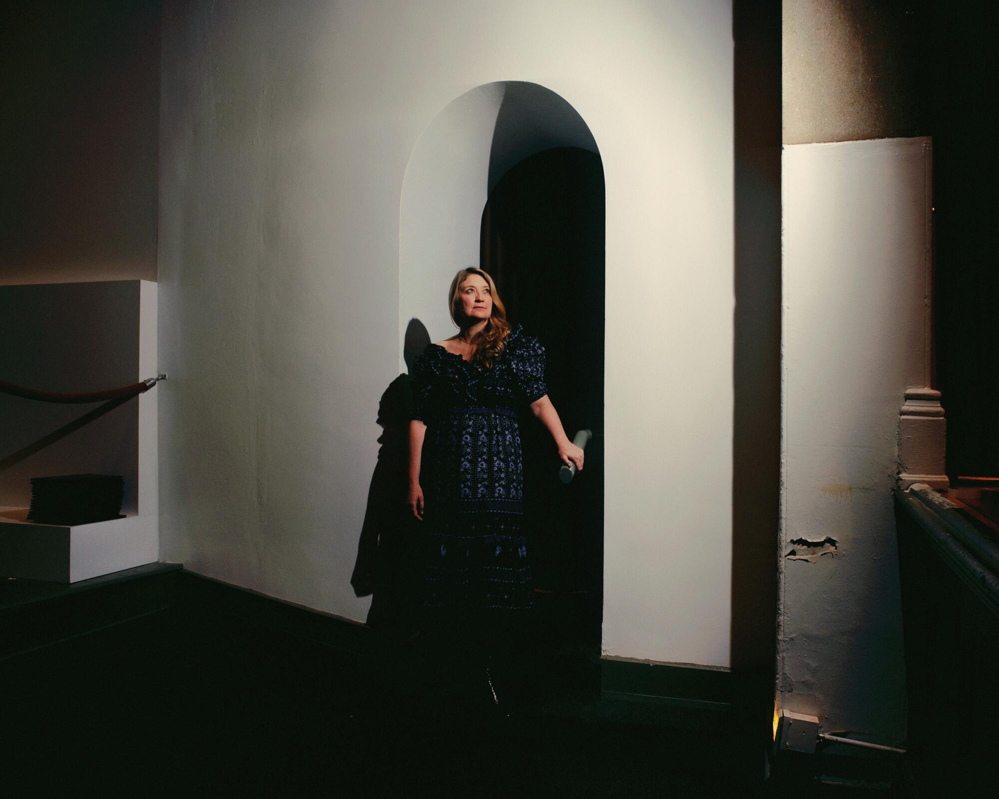 A woman poses under an arched doorway holding a handrail