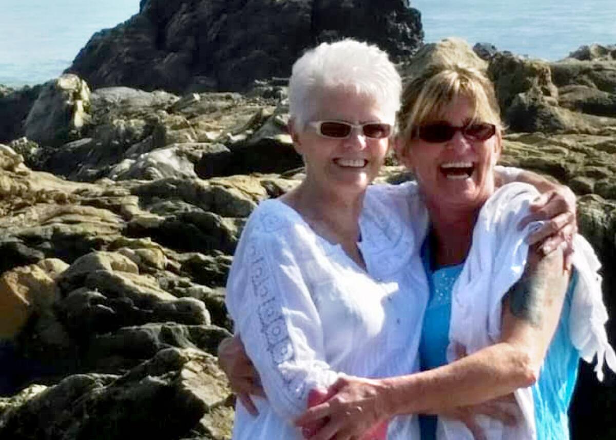 Two women pose for the camera near a rocky coast. They are hugging and laughing. 