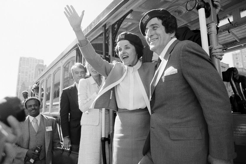 FILE - San Francisco Mayor Dianne Feinstein and singer Tony Bennett, who sang "I Left My Heart in San Francisco," hangs on to the outside of a cable car in San Francisco before taking a test ride, Wednesday, May 2, 1984. (AP Photo/Jeff Reinking, File)