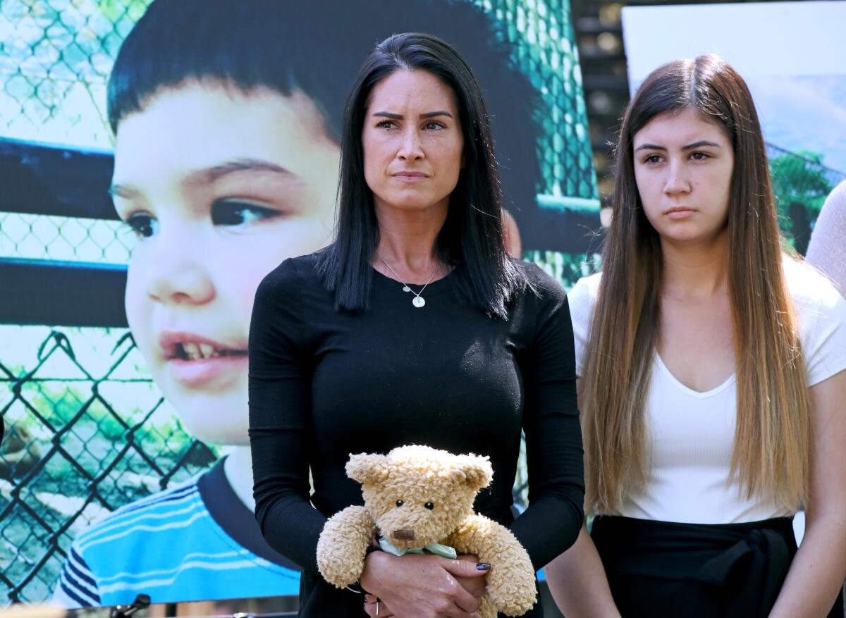 Two people, one holding a teddy bear, stand before a large photo of a child.